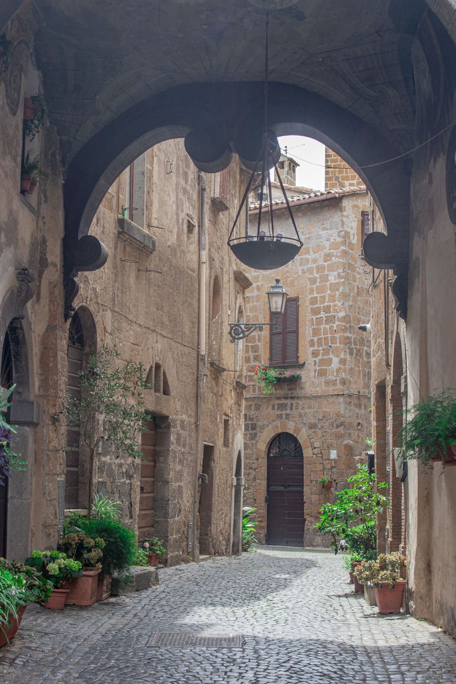 A cobbled lane in Orvieto's old town beneath a stone arch, with potted plants along the walls